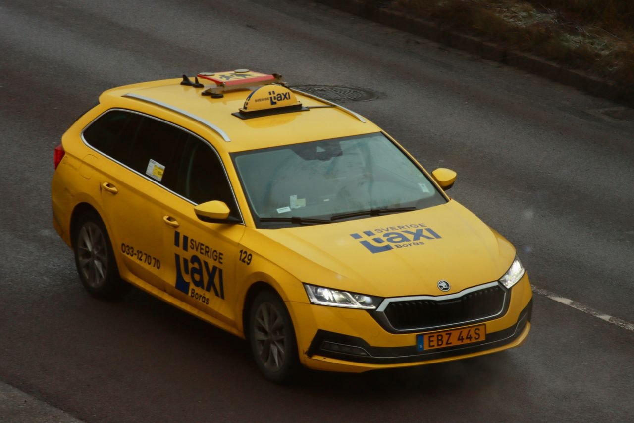 A bright yellow taxi driving on a city road, captured from above, with clear branding.