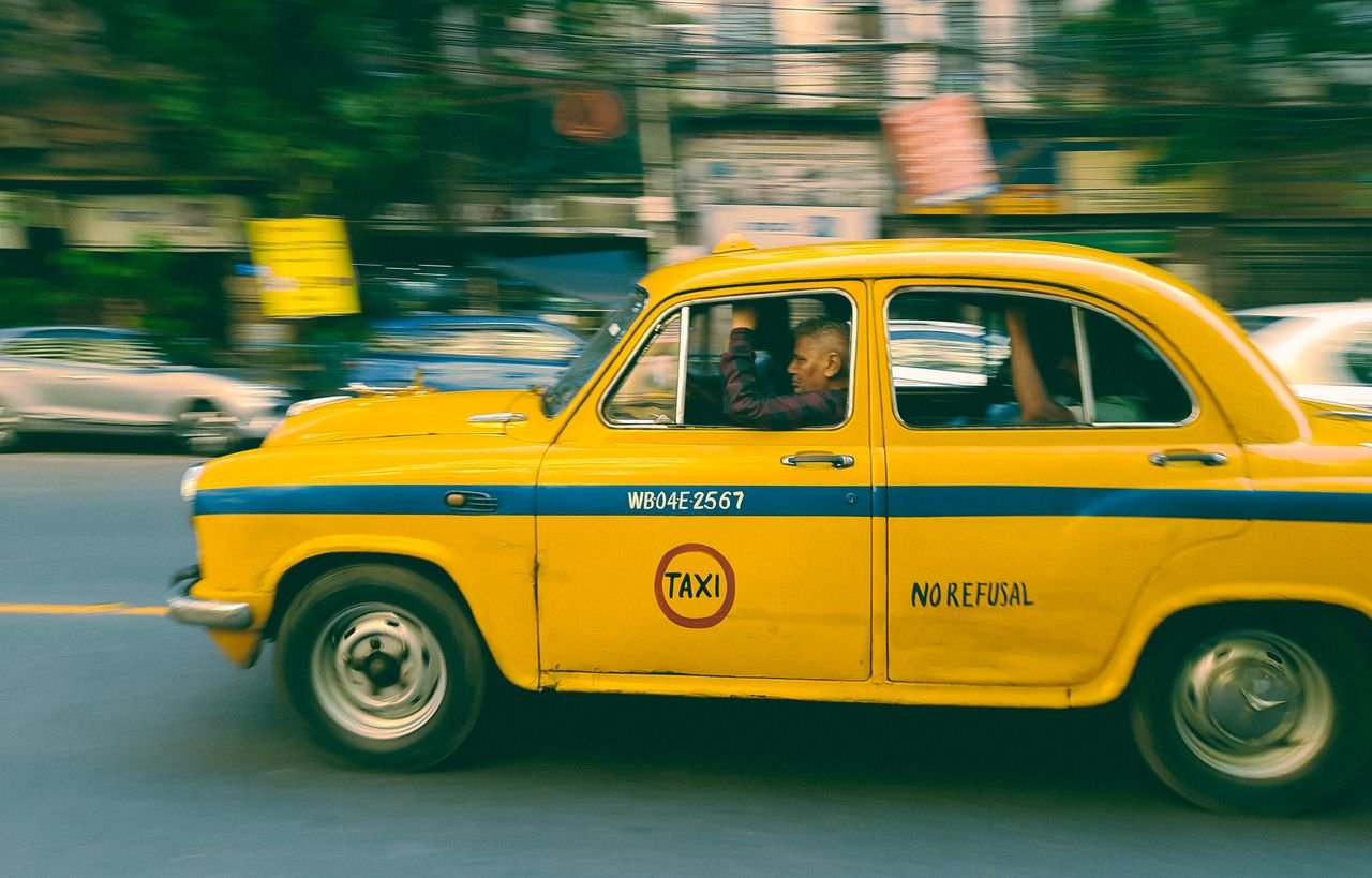 A vibrant yellow taxi speeds through a bustling Kolkata street, capturing urban life.