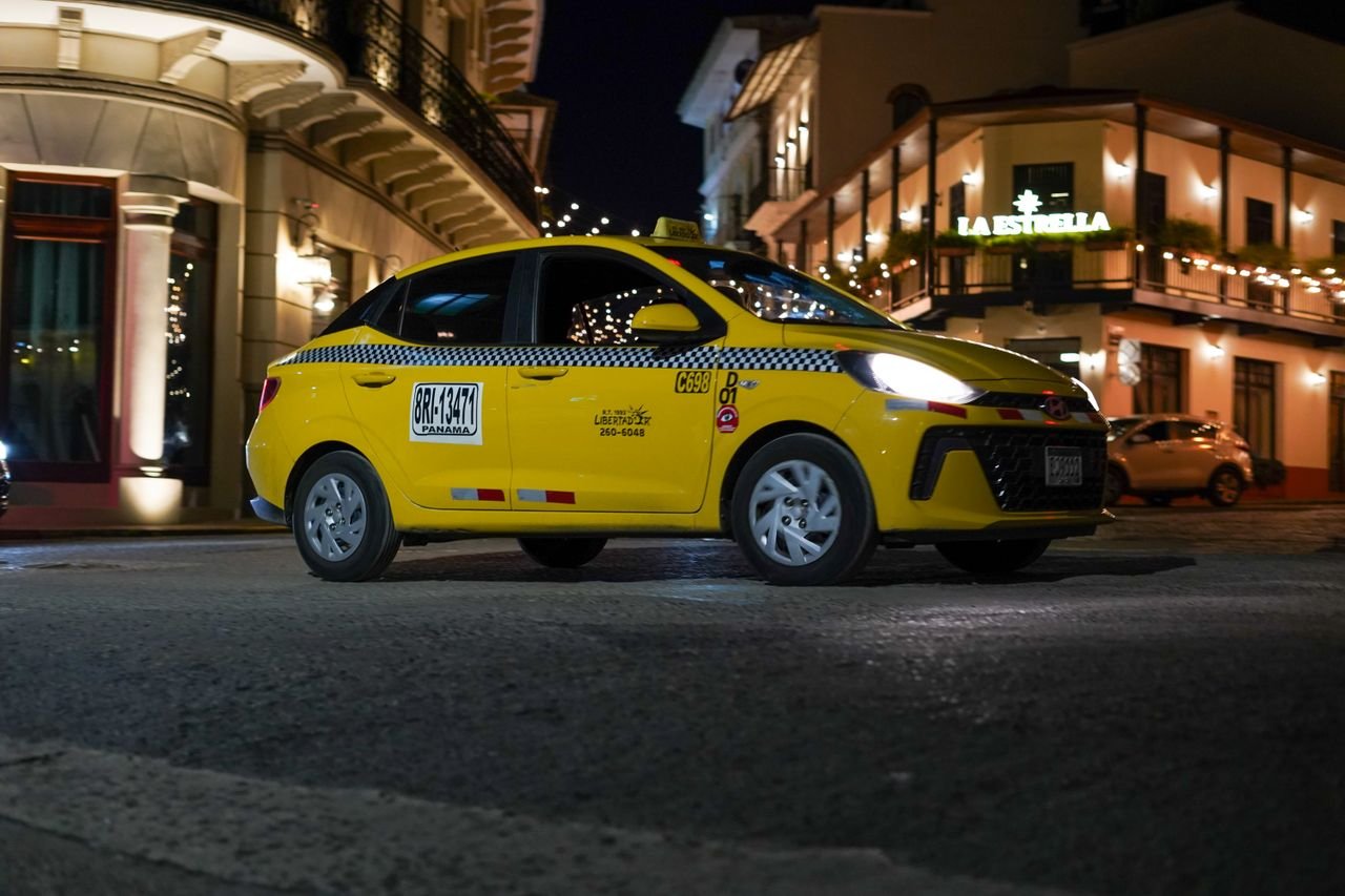 A yellow taxi drives through a beautifully lit street at night, showcasing urban life.