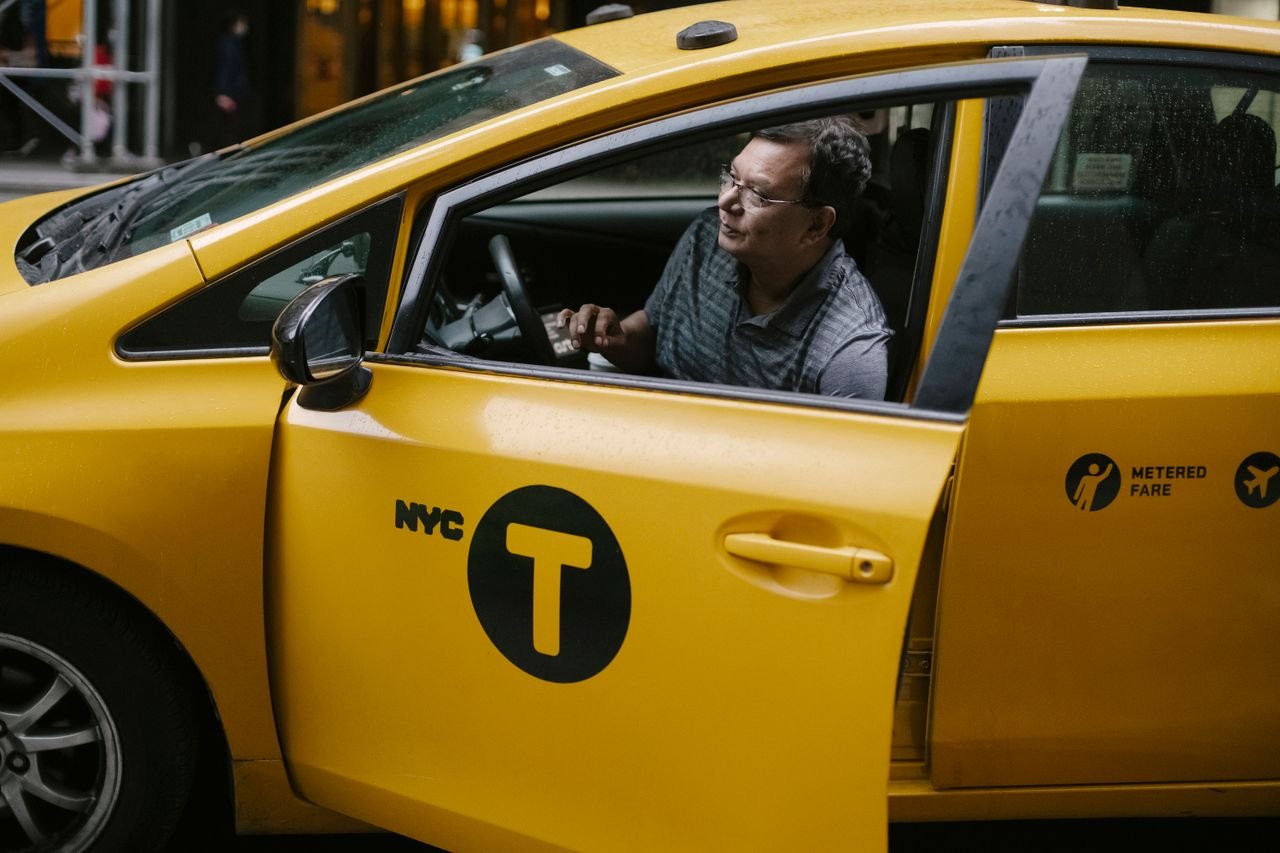 Crop ethnic taxi driver wearing sunglasses opening yellow taxi car door in New York